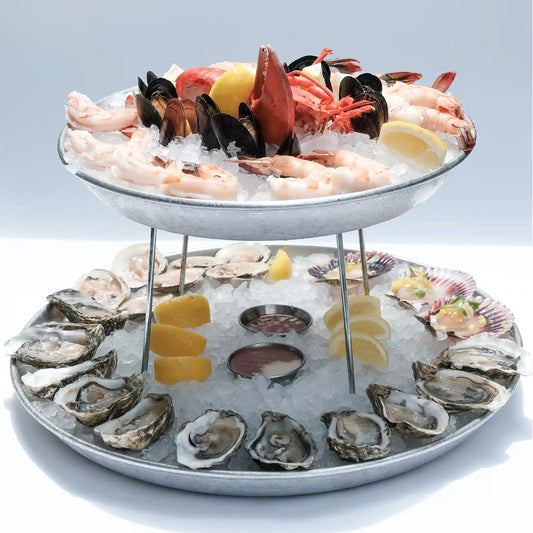 Deluxe two-tiered seafood platter on ice with oysters, shrimp, crab legs, mussels, and dipping sauces.